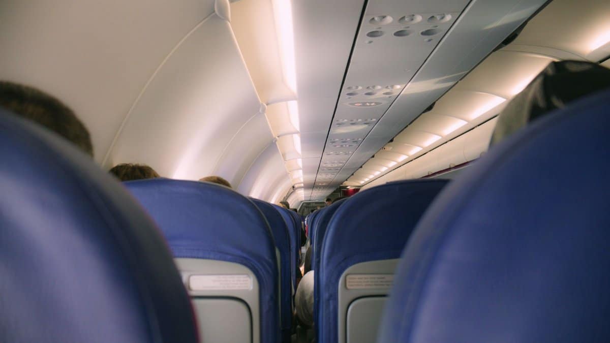 A view of a modern airplane cabin showing rows of blue seats and overhead compartments.