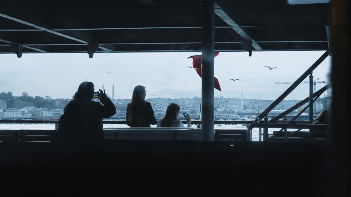 Passengers silhouetted on a ferry in Istanbul with cityscape background.