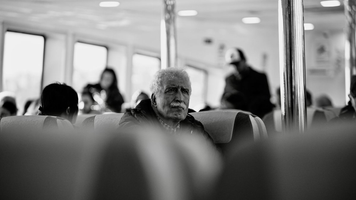 Black and white candid shot of an elderly man sitting on public transport, reflecting a contemplative mood.