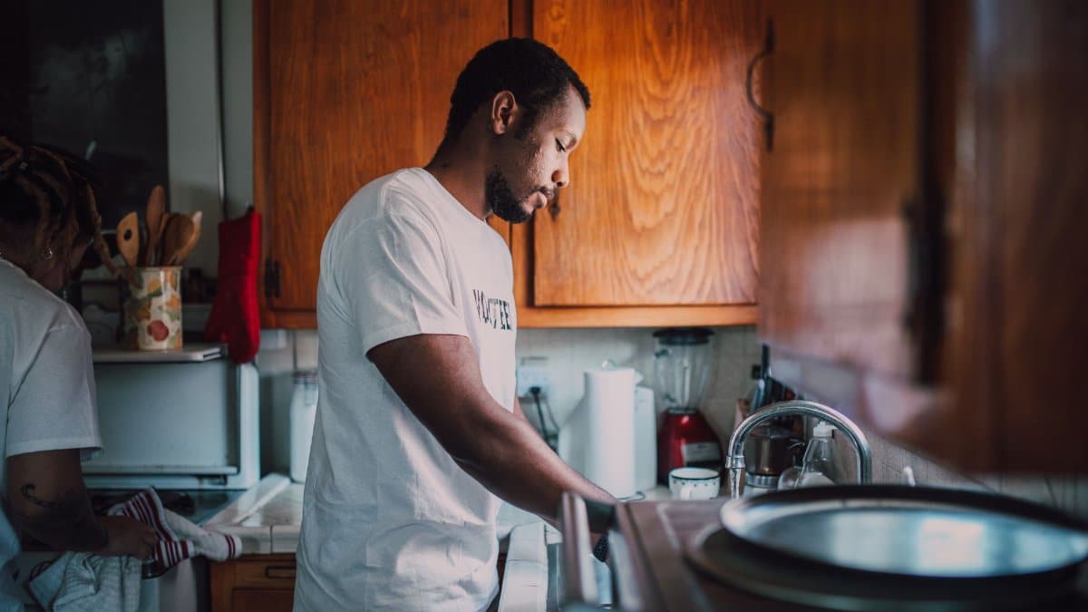 A man and woman volunteer wash dishes in a kitchen, helping their community.