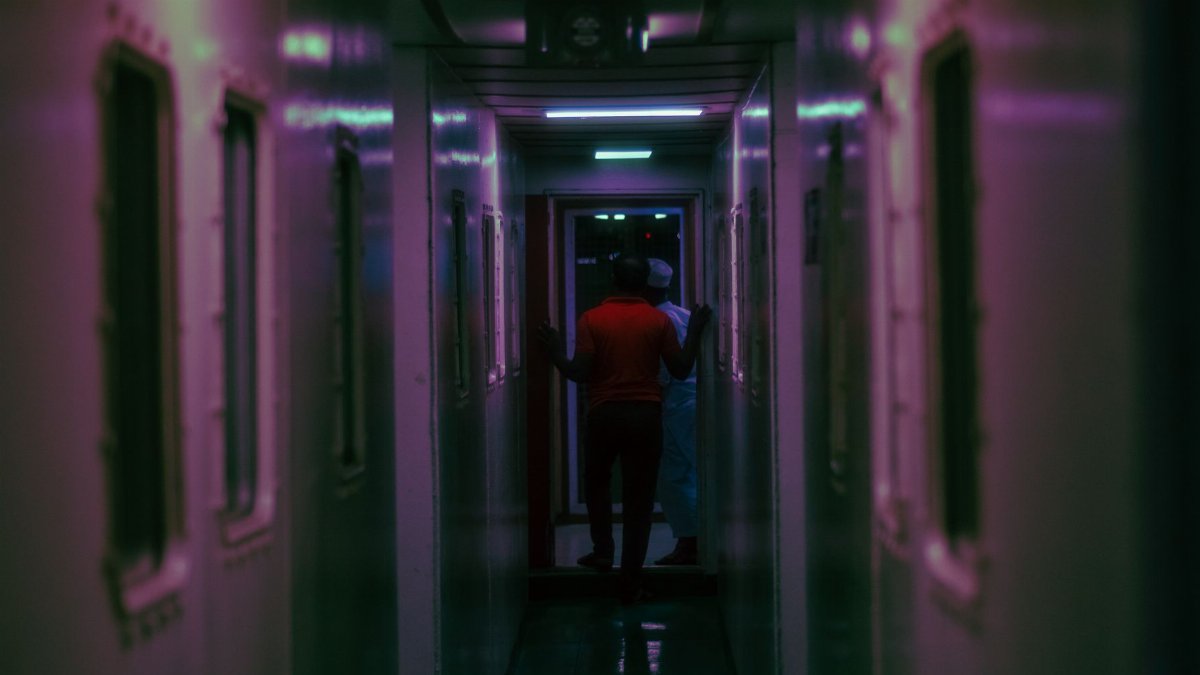 Moody dimly lit corridor inside a building with two figures seen from the back.