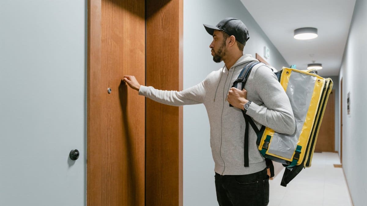 A food delivery man knocks on an apartment door, carrying a thermal bag.