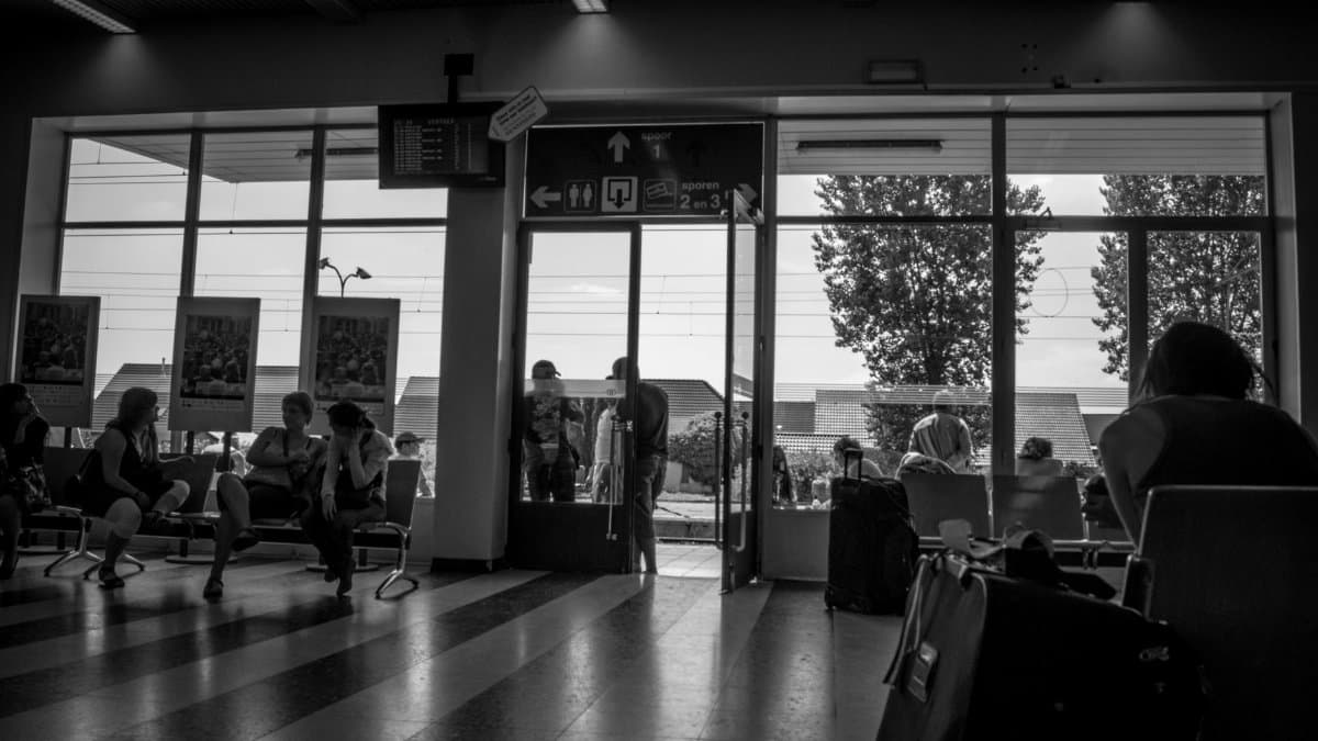 Monochrome view of people sitting and waiting inside a station lobby.