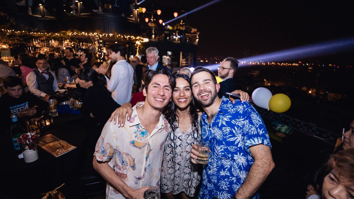 Vibrant night party with friends enjoying drinks and lights on a rooftop venue.