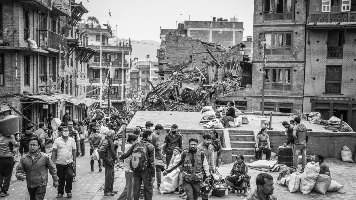 Grayscale photo showing earthquake aftermath in Bhaktapur, with people amidst debris and damaged buildings.