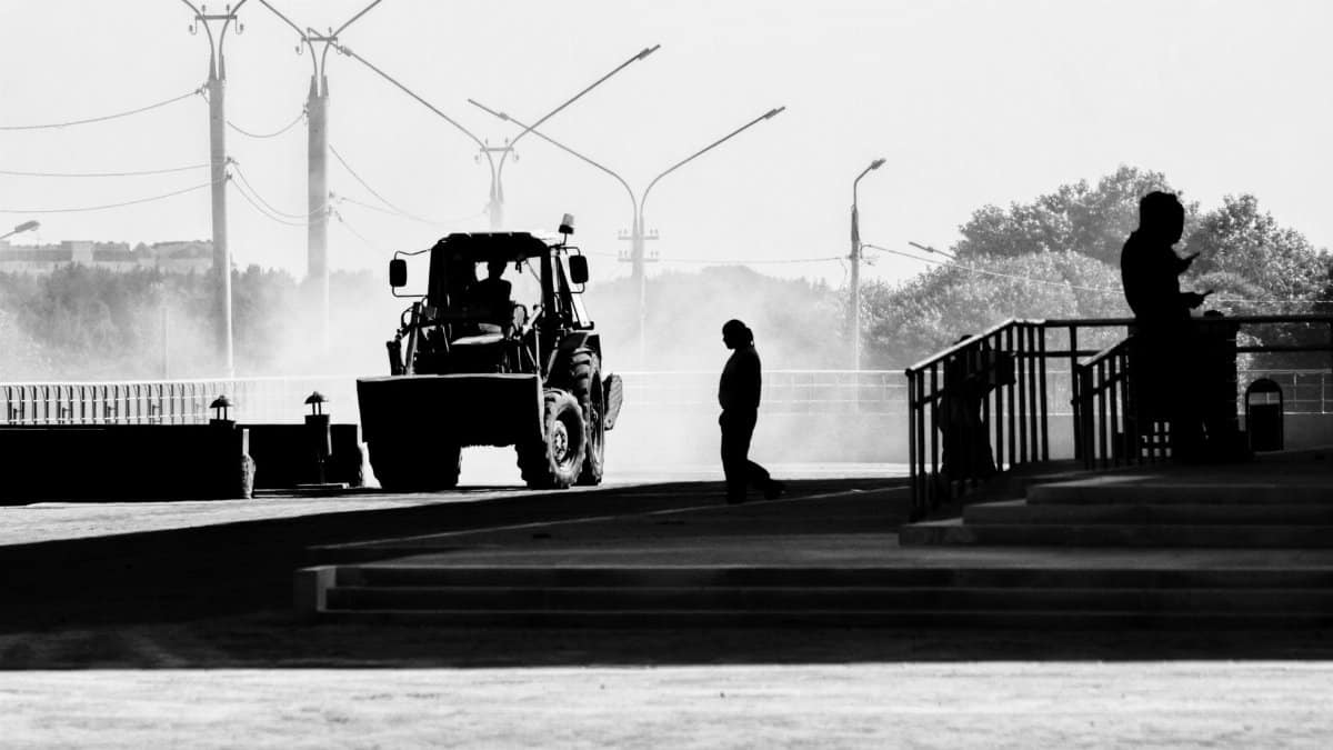 A dramatic black and white scene shows silhouettes of people and a tractor on a dusty city street.