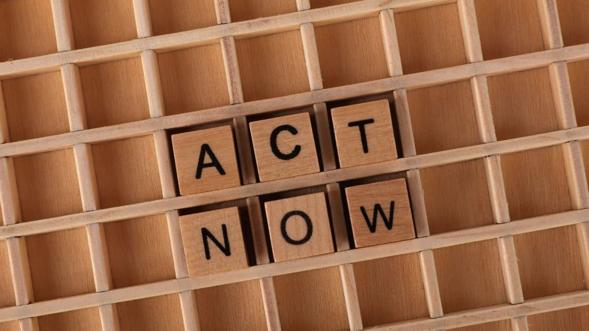 Wooden letter tiles forming the phrase 'Act Now' on a wooden grid background.