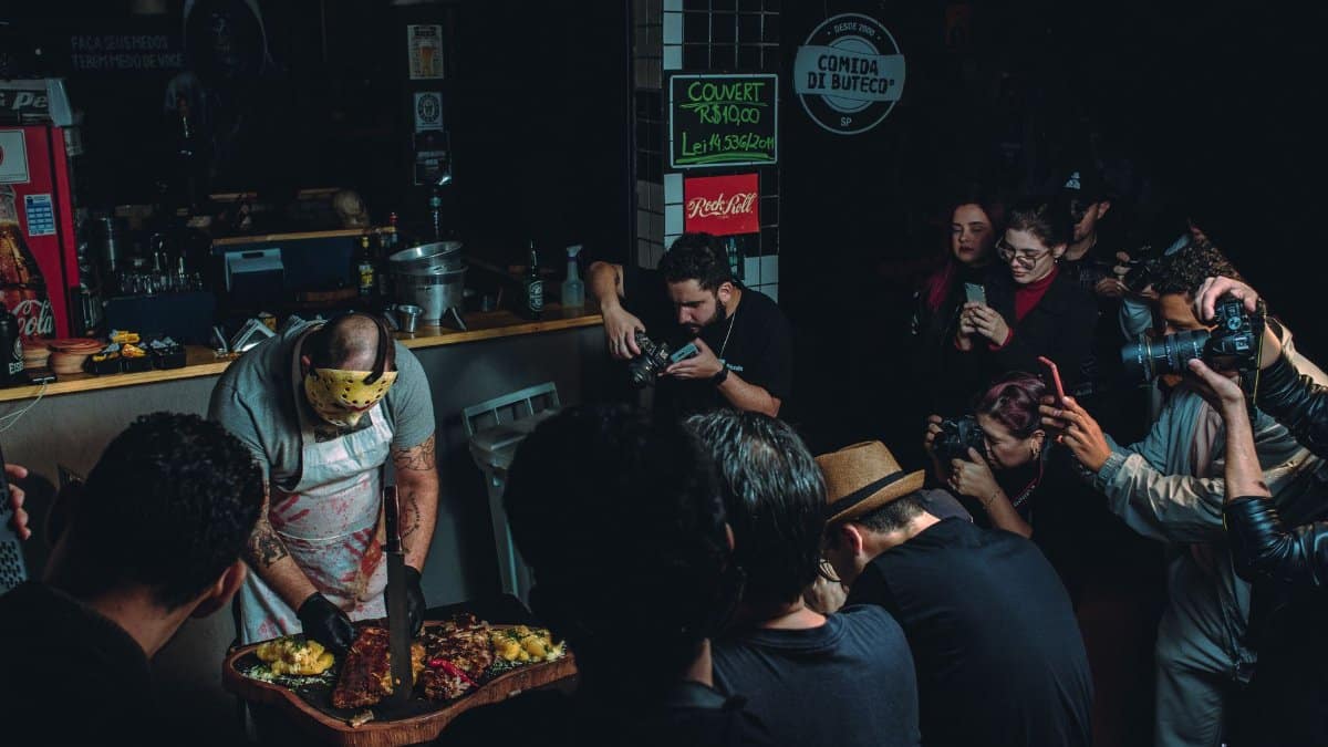 A chef prepares a meal while being photographed by a group in a dimly lit restaurant.