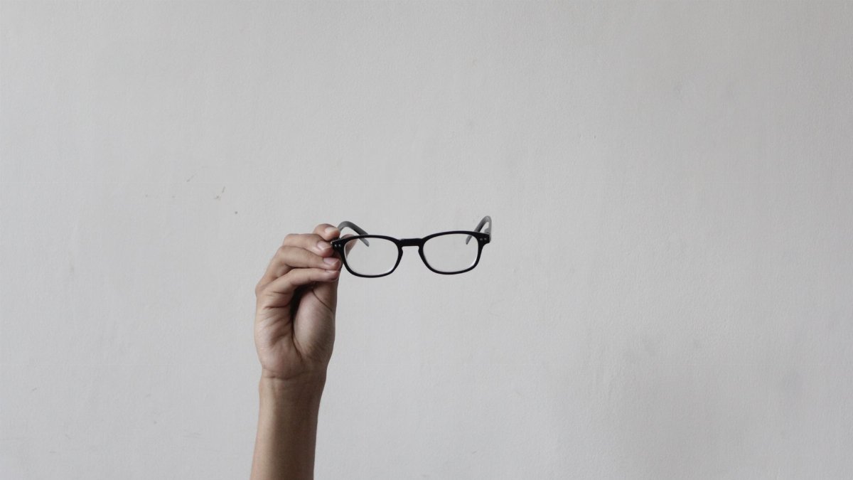Close-up of hand holding eyeglasses against a plain background.