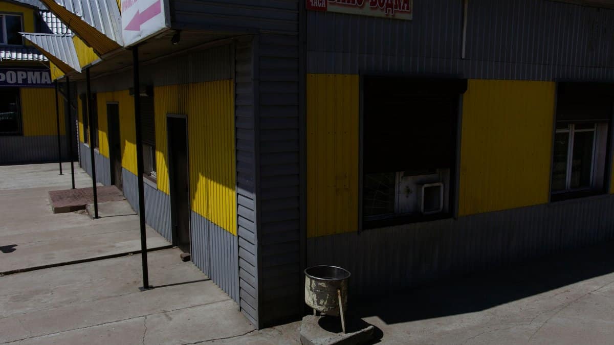 Exterior view of a yellow and gray industrial building in sunlight with shadows.