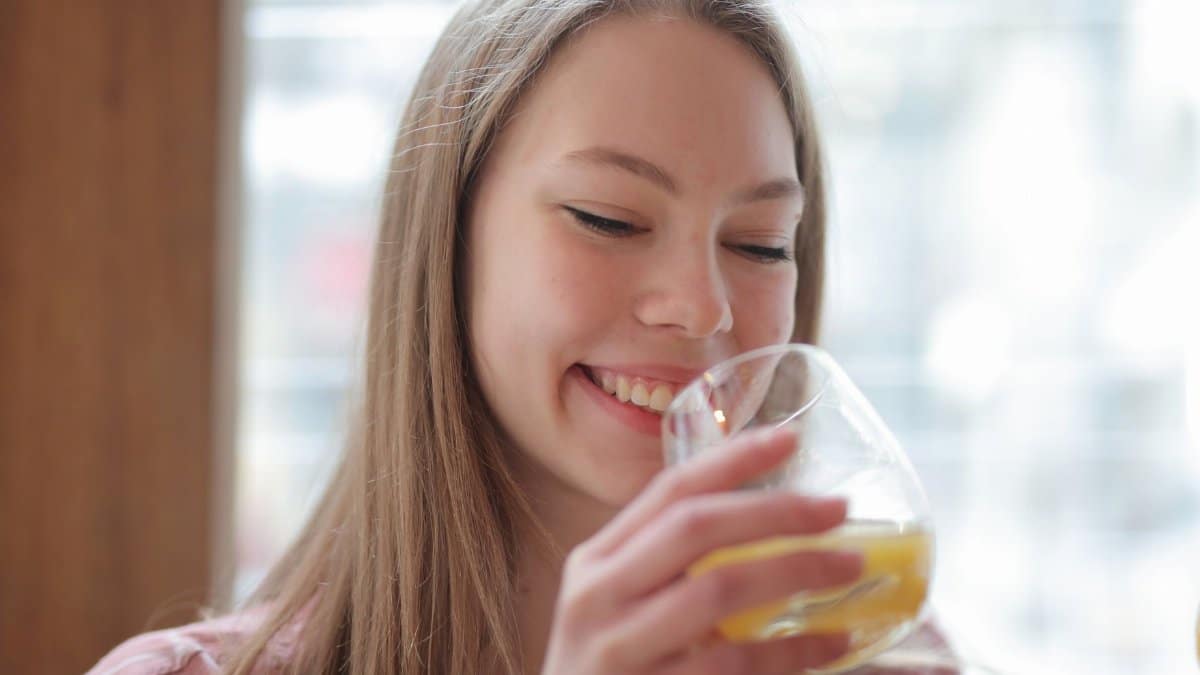Young woman smiles while enjoying a glass of fresh orange juice indoors.