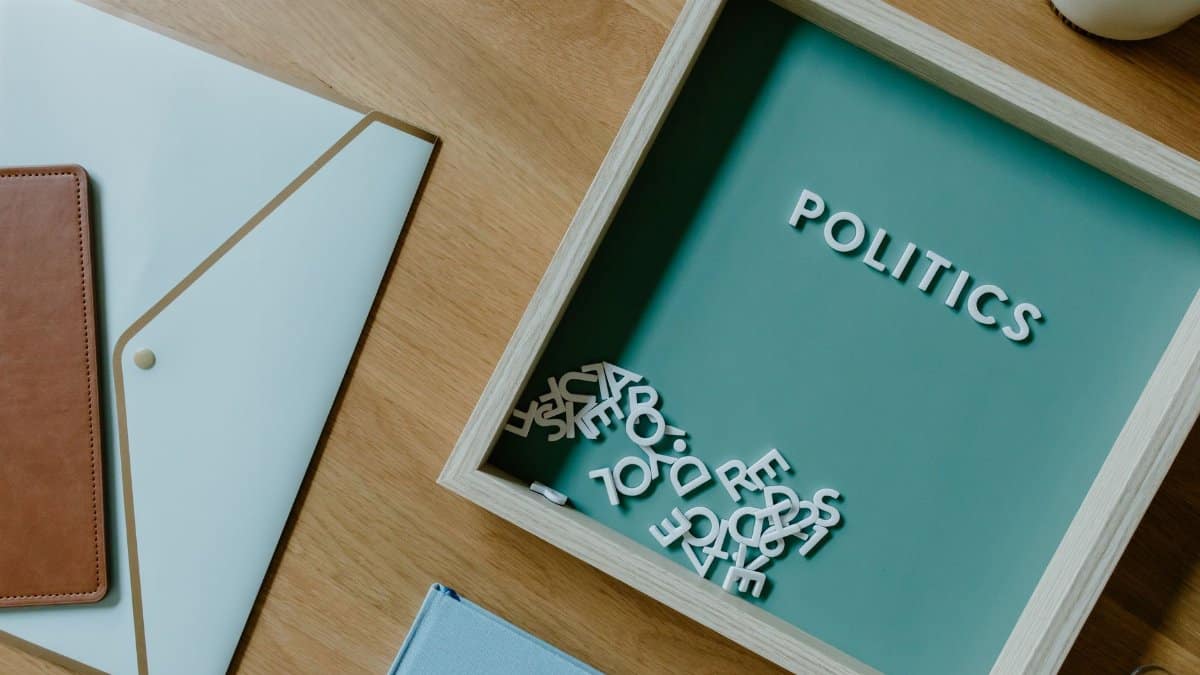 Top view of a box with 'POLITICS' text alongside office items on a wooden desk.