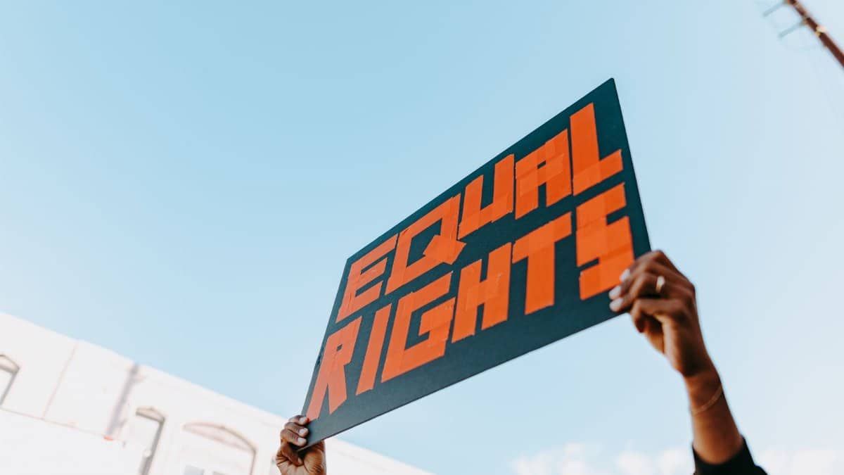 Hands holding a bold equal rights sign at an outdoor protest.