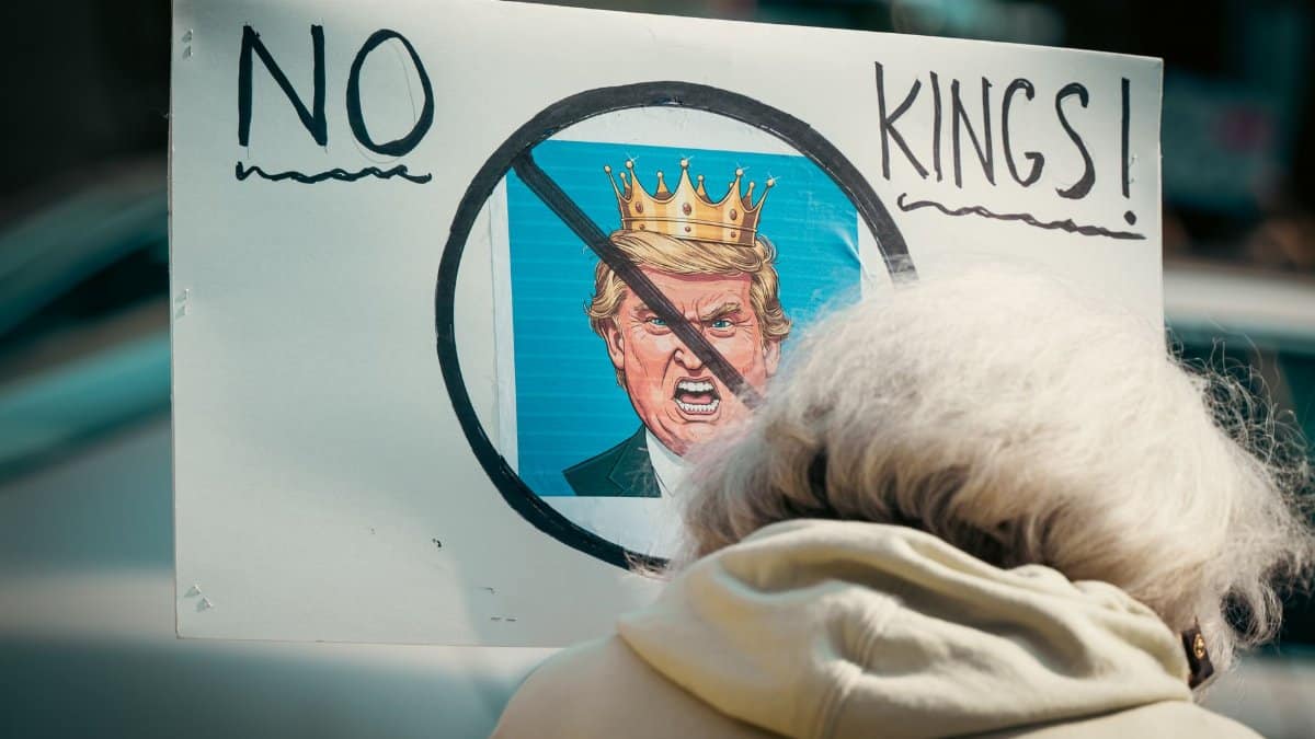 A protest sign reading 'No Kings' depicts resistance against monarchy with a satirical image.