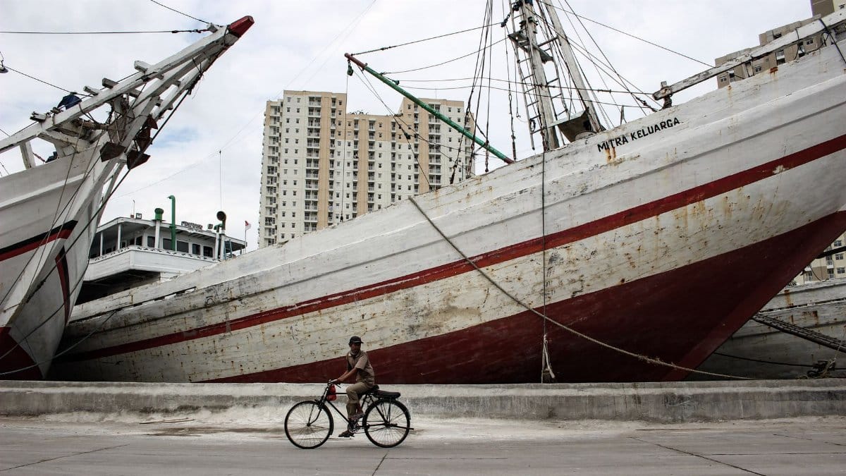 A man cycles in front of large, docked ships at an urban port, blending modern life with maritime history.