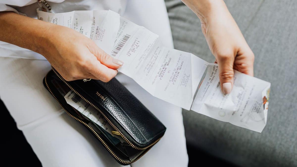 Close-up of a woman's hands managing multiple receipts taken from a black wallet.