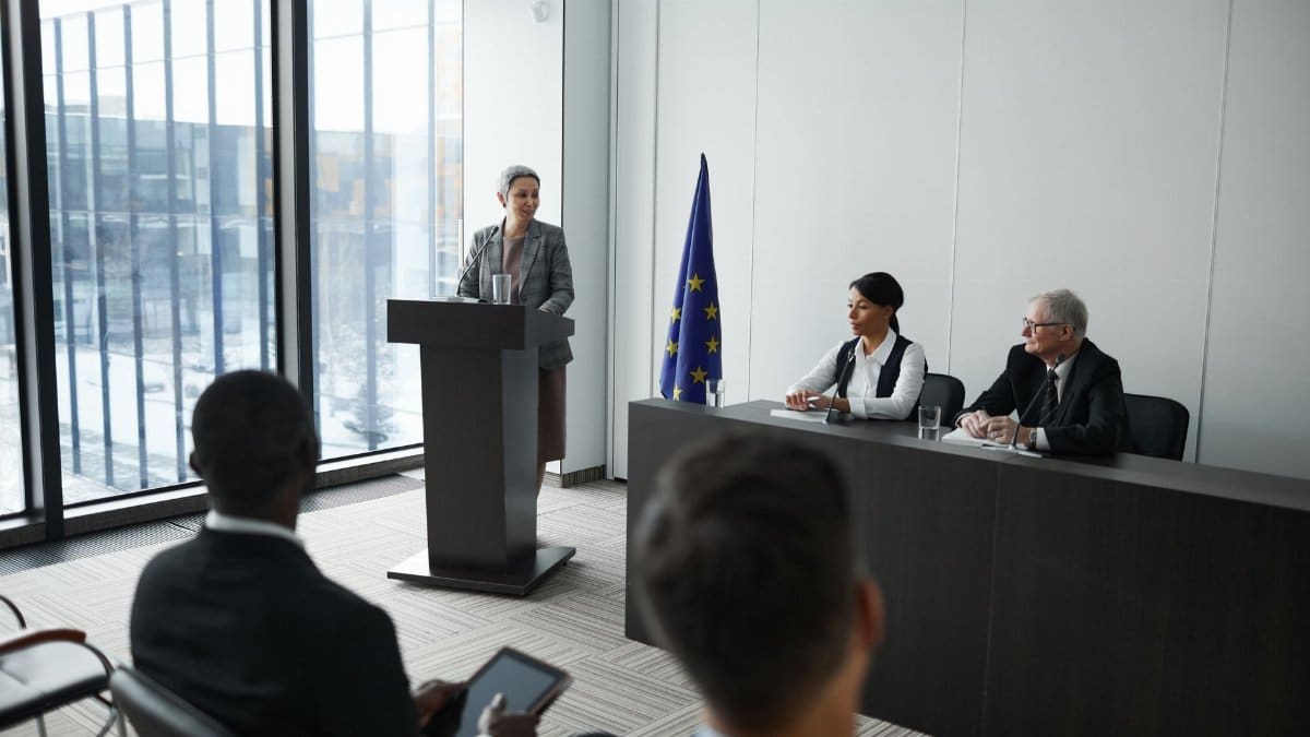 Professional conference setting with a speaker at a podium and attentive audience in a modern meeting room.