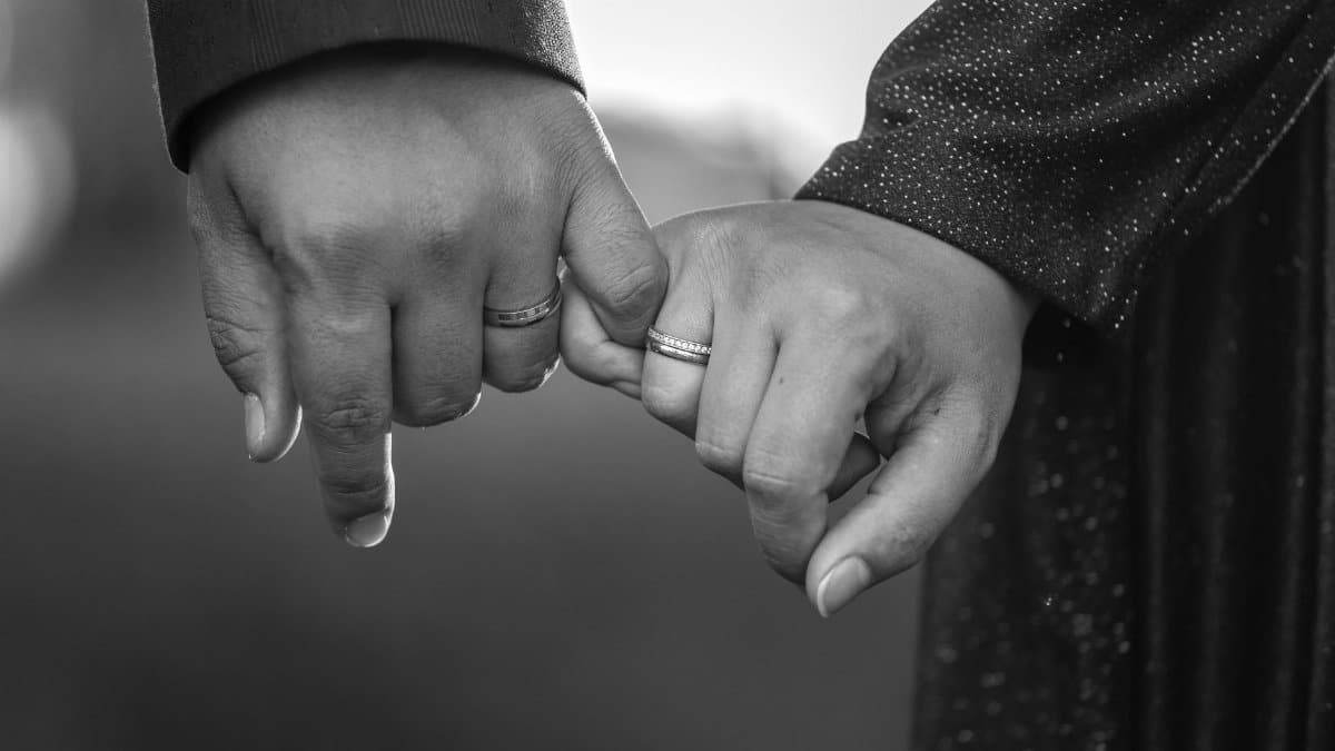 Black and white image of couple holding hands, showcasing engagement rings, symbolizing commitment and love.