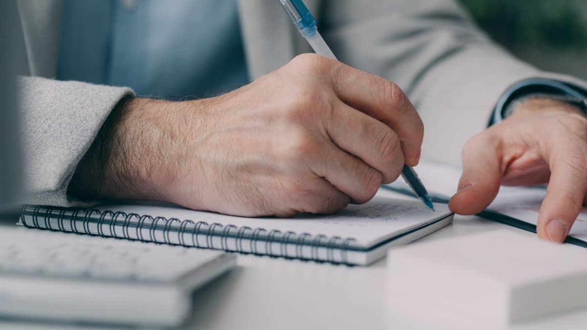 Close-up of a businessman taking notes in a notebook at a desk.