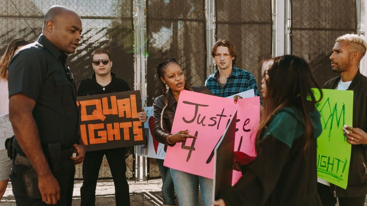 Protesters holding signs demand justice and equal rights in street confrontation with a policeman.