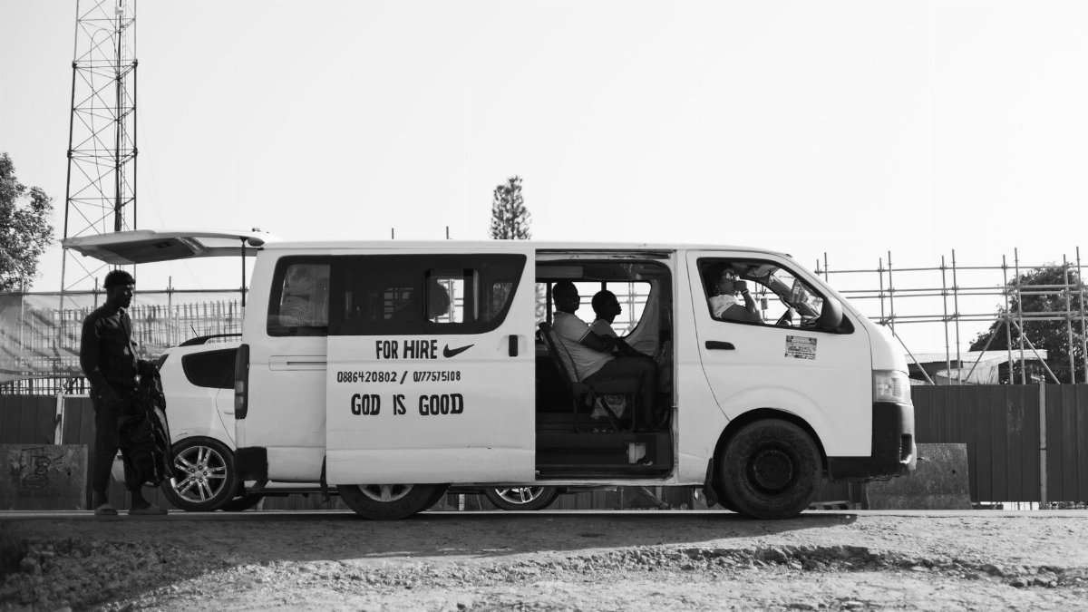 Street view of a minivan for hire with people inside in urban setting.