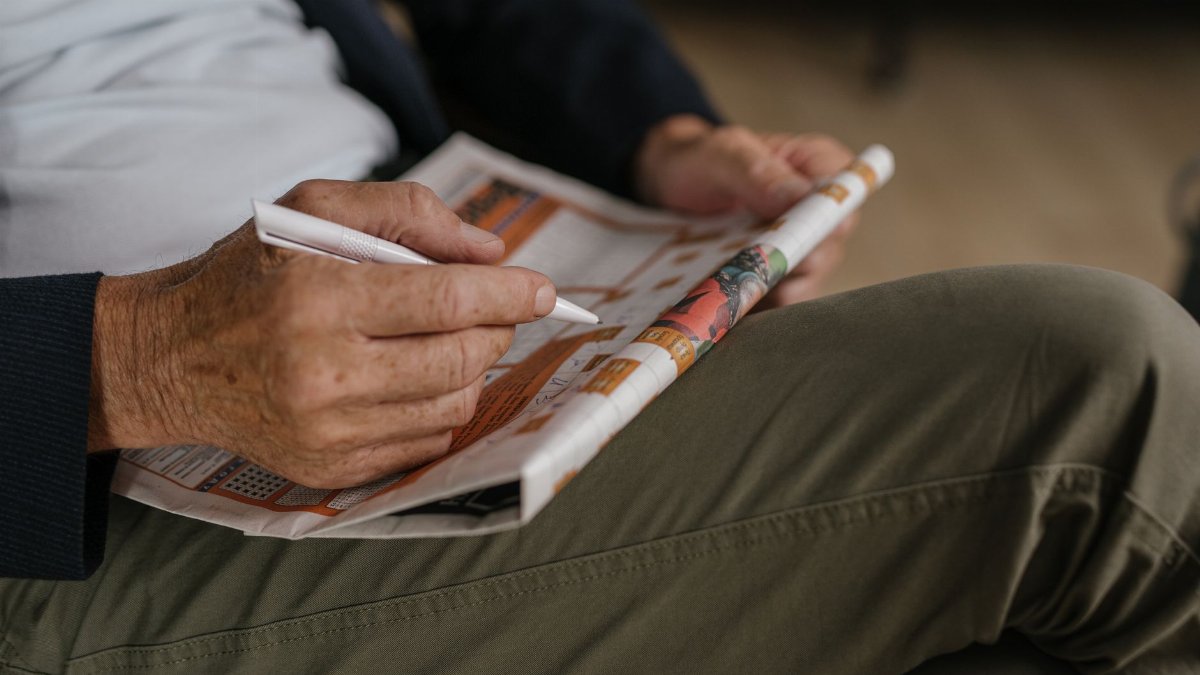 Close-up of a senior adult solving a crossword puzzle in a newspaper with a pen.