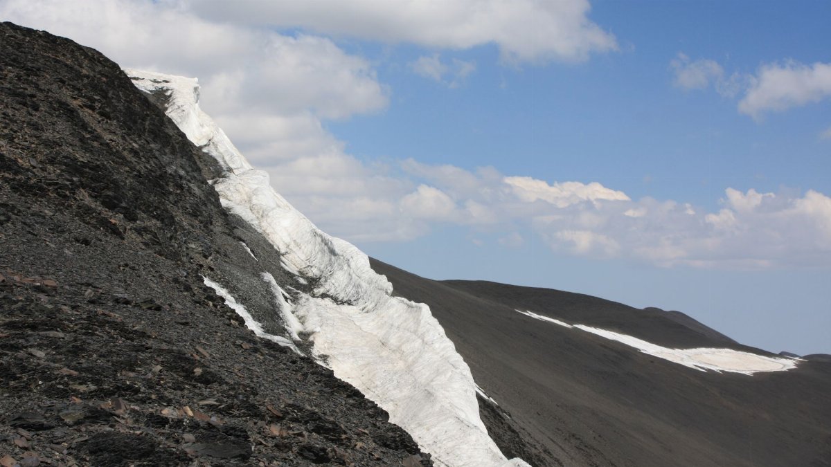 A dramatic icy mountain ridge captured under a clear blue sky with fluffy clouds.