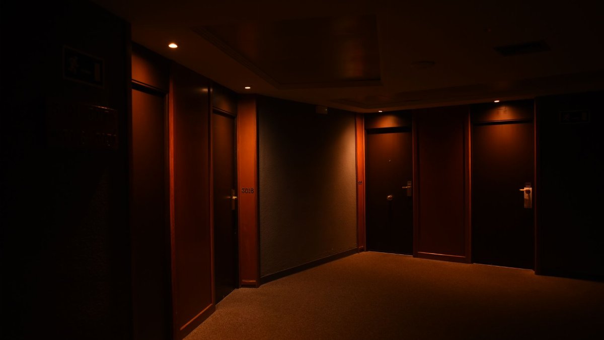 A dark, quiet hotel corridor featuring multiple closed wooden doors and soft lighting.