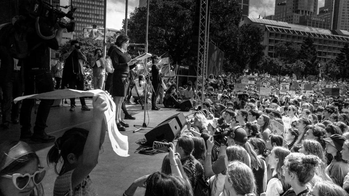 A large crowd at an outdoor gathering in Sydney, featuring a public speaker on stage.