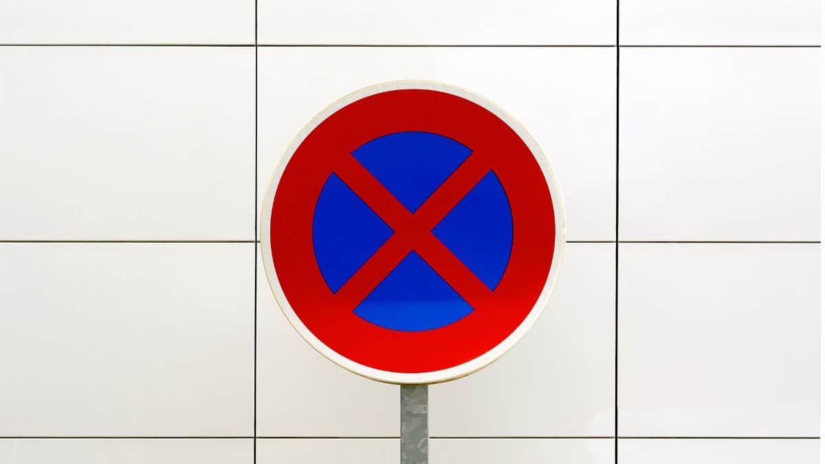 Close-up image of a red and blue no stopping traffic sign against a tiled white background.