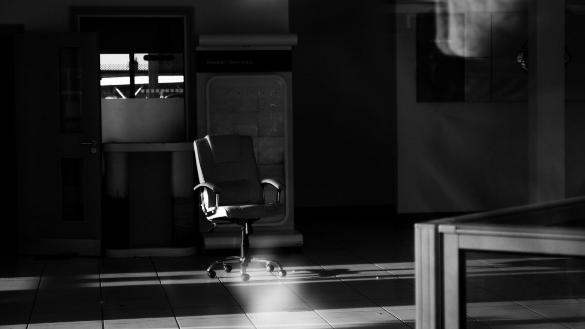 A black-and-white photo of an empty office space with a single chair and dramatic lighting.