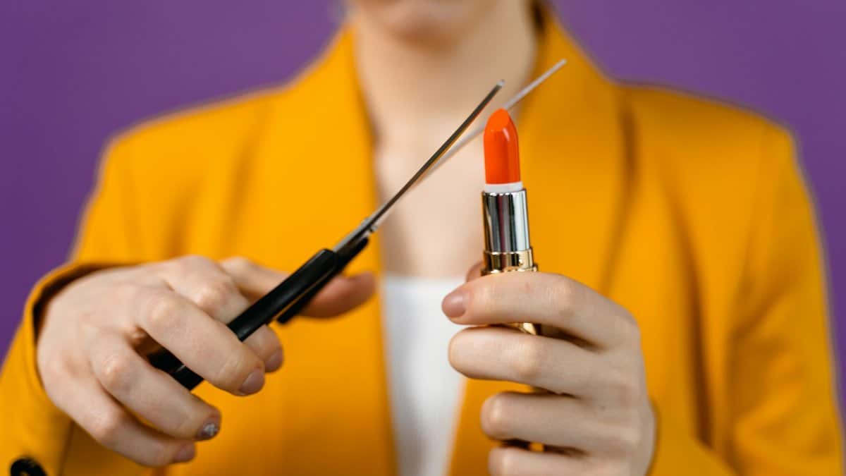 Close-up of a woman holding lipstick being cut with scissors, showing bold color contrast.