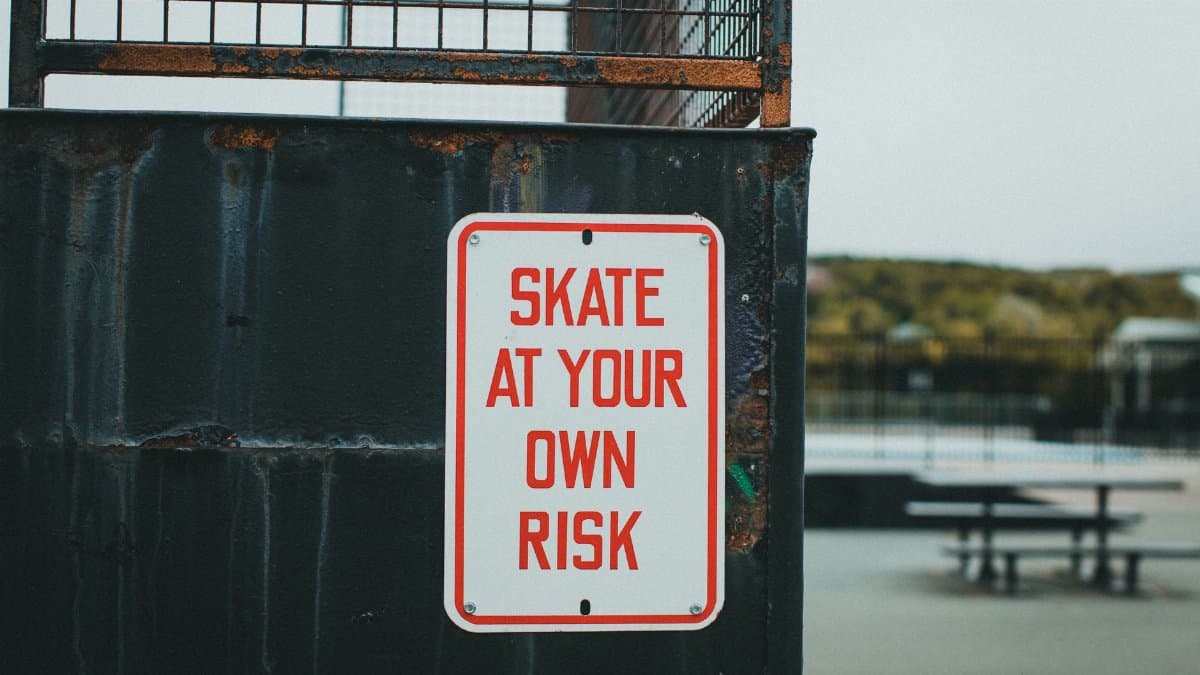 Close-up of a 'Skate at Your Own Risk' sign at outdoor skate park.