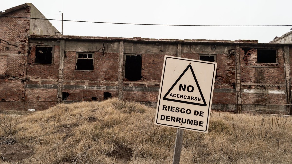 An abandoned brick building with a warning sign indicating risk of collapse in Spanish.