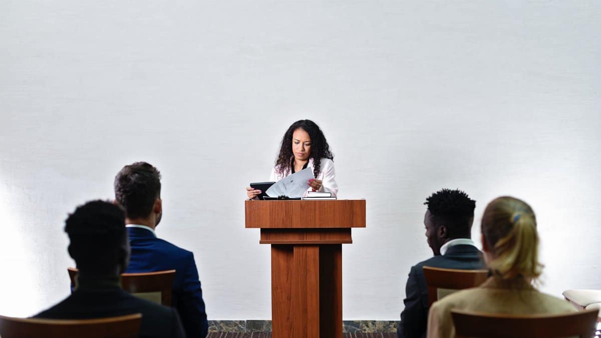 Confident woman delivering a speech to a diverse audience in a conference room.