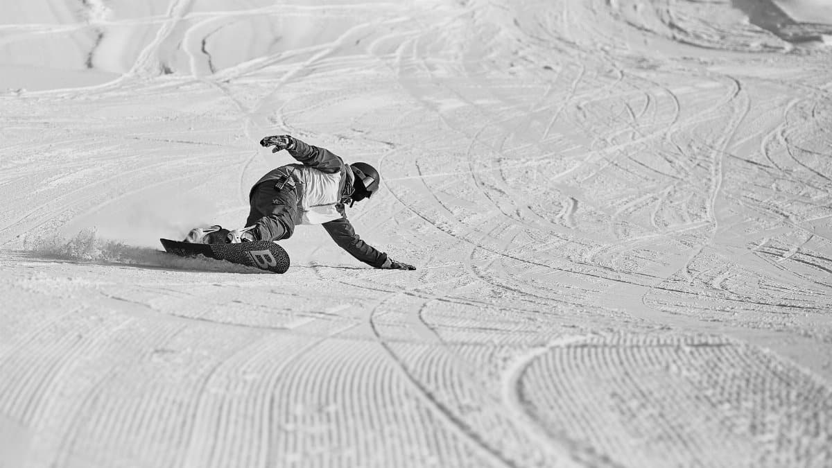 From above of anonymous snowboarder in helmet and protective equipment sliding down on snowy slope