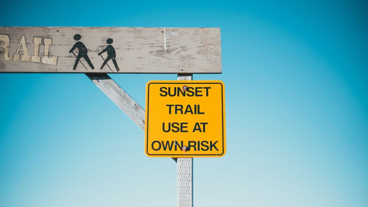 Yellow signboard with warning inscription and wooden arch on background of blue sky