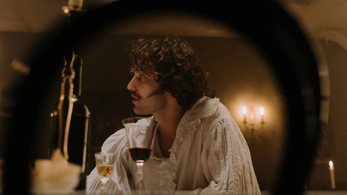 A man in period costume enjoys a candlelit dinner with wine, creating an atmospheric vintage portrait.
