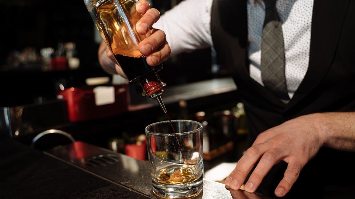 Close-up of bartender pouring whiskey into a glass at a bar counter.