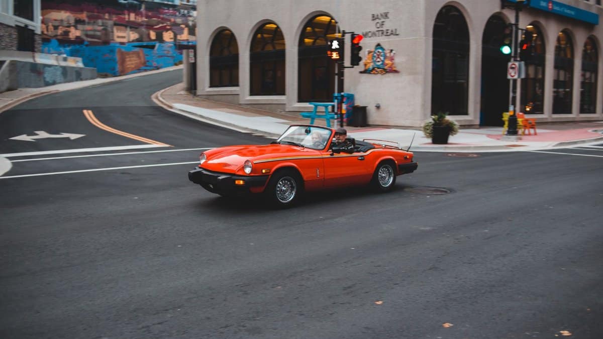 Anonymous couple in bright luxury vintage auto driving on asphalt roadway near urban buildings during trip