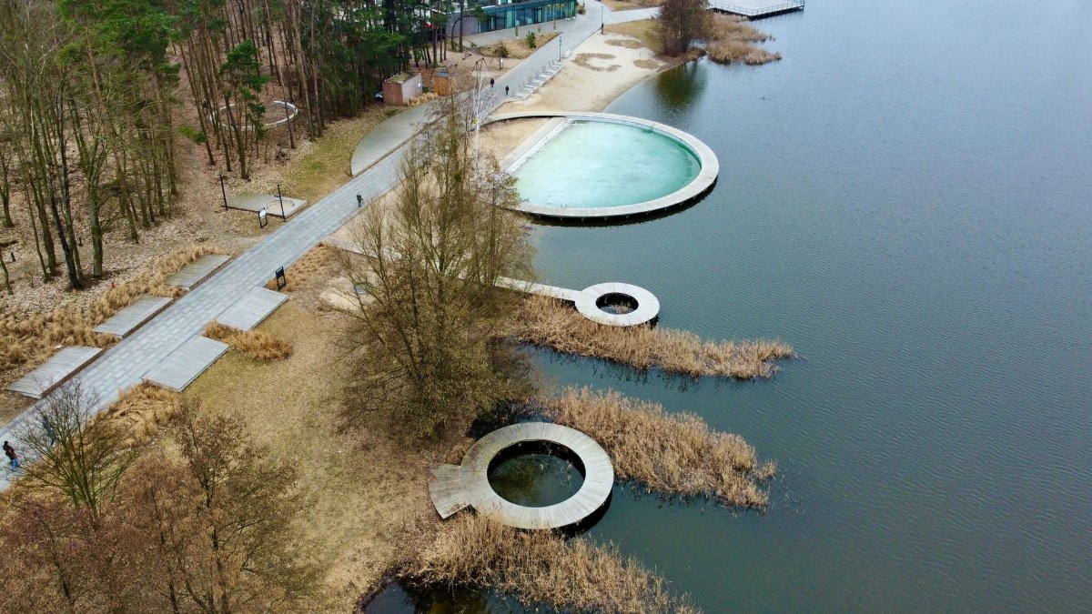 Aerial shot of a contemporary park with circular piers over a calm lake surrounded by trees.