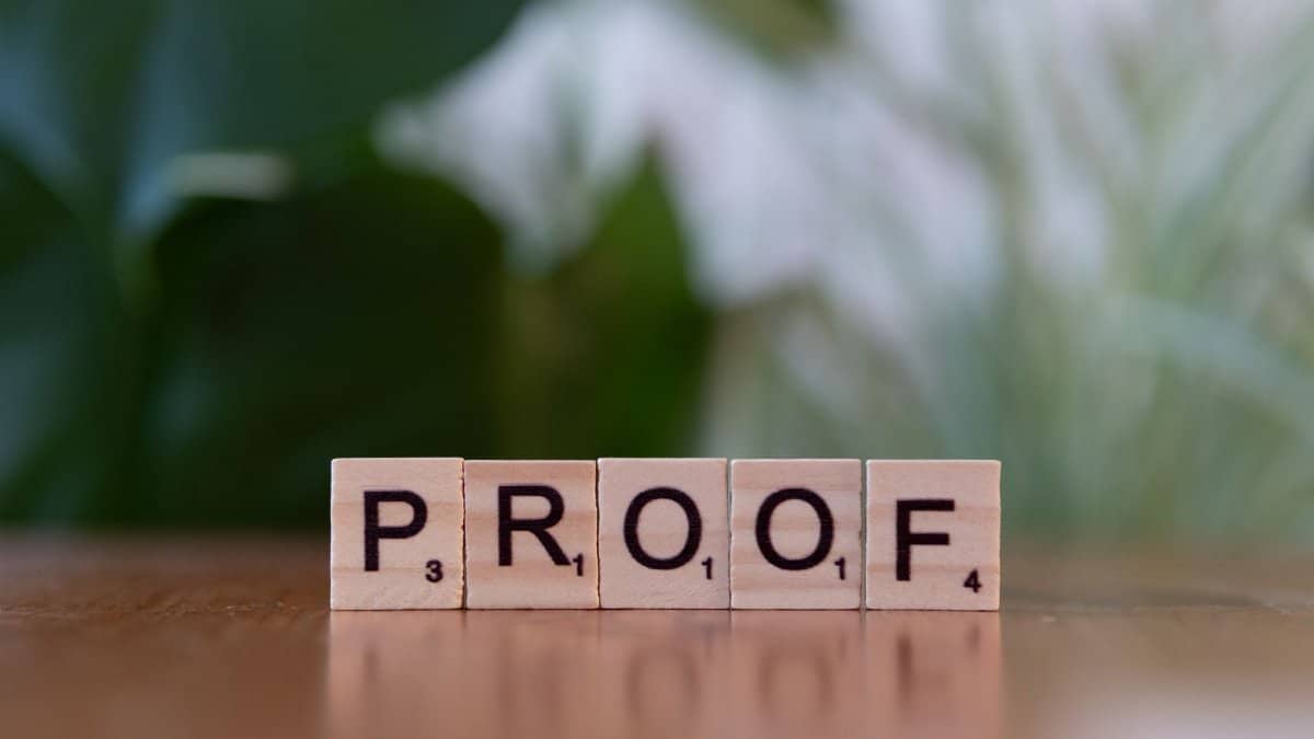 Wooden Scrabble tiles spelling 'PROOF' on a wooden table with green background.