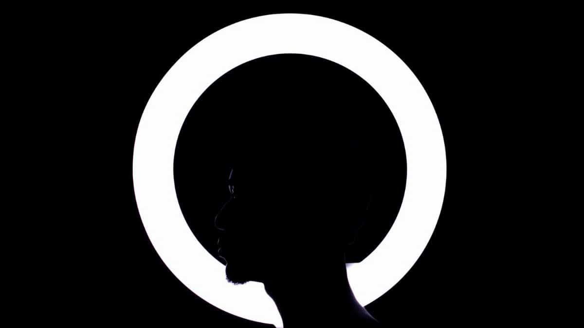 Profile silhouette of a man with glowing ring light creating a dramatic halo effect in darkness.