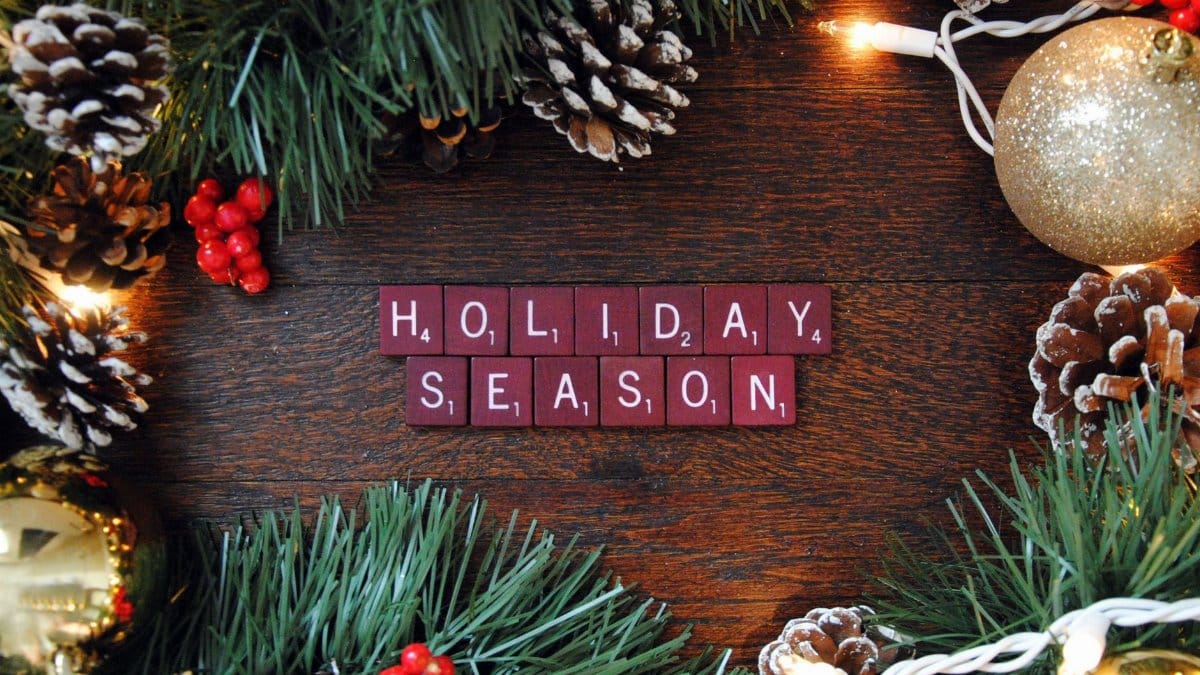 Top view of festive Christmas decorations with Scrabble tiles spelling 'Holiday Season' on a wooden surface.