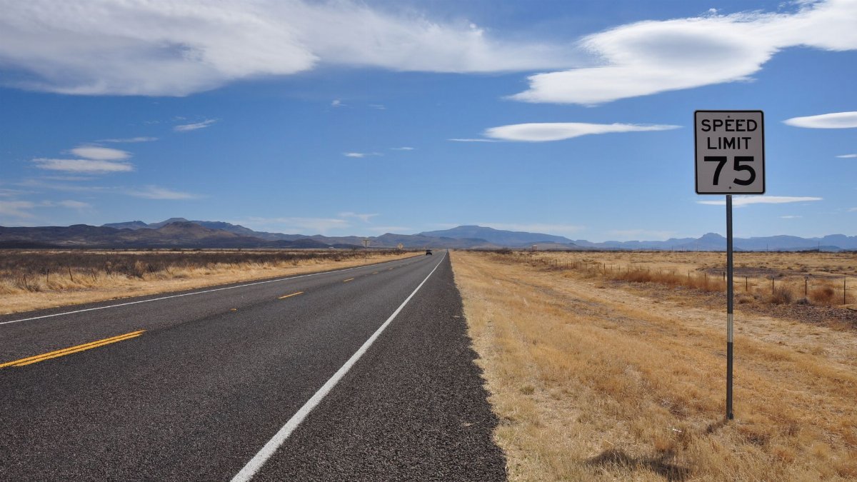A deserted highway stretches into the horizon under a bright blue sky with a speed limit sign in the countryside.
