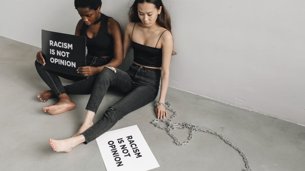 Two women holding placards stating 'Racism is not opinion' with chains on the floor.
