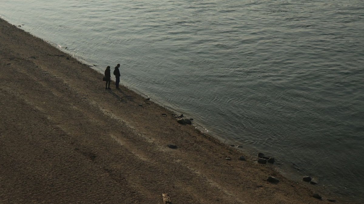 Silhouettes of two people standing on the Danube River shore in Budapest, creating a serene scene.