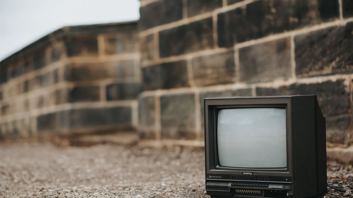 Black old fashioned television placed on ground near concrete fence in city on street against cloudless sky on blurred background