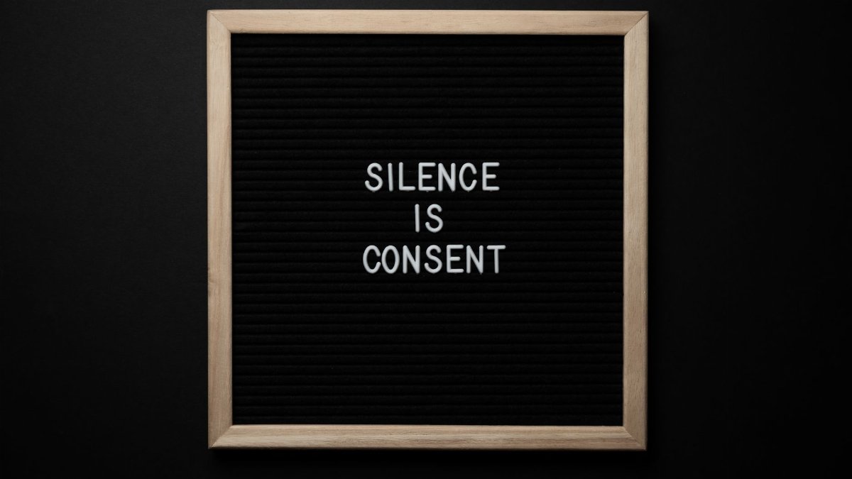 From above blackboard with written phrase SILENCE IS CONSENT on center on black background