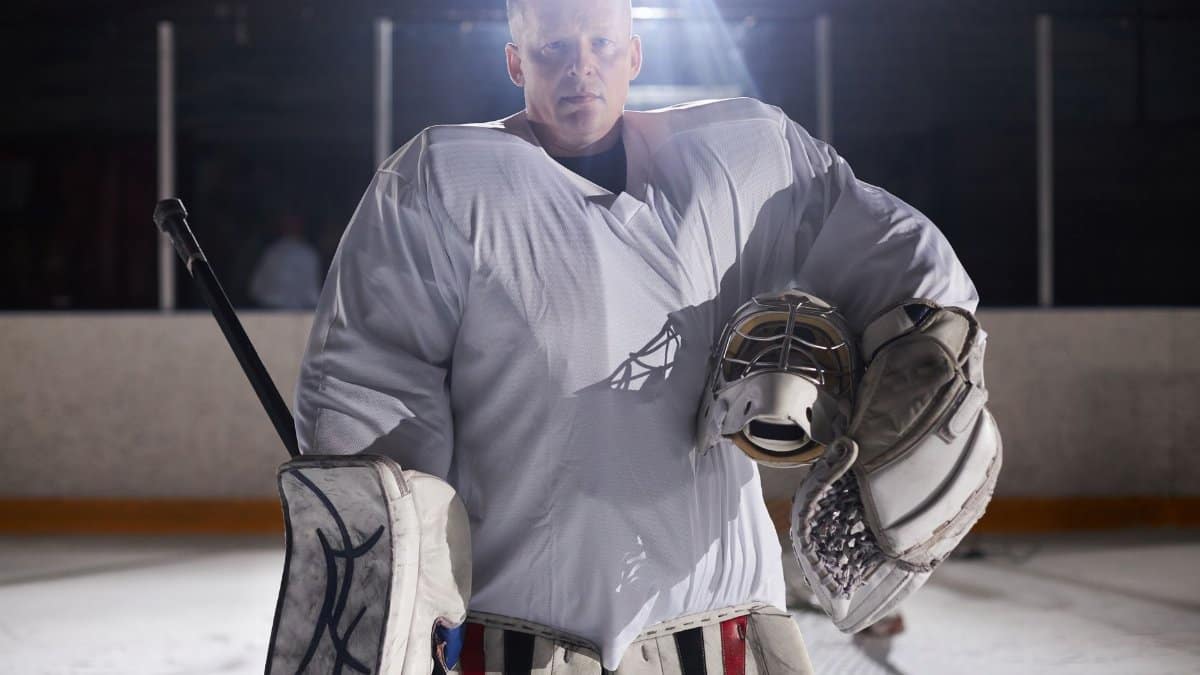Focused ice hockey goalie stands confidently in full gear on an indoor ice rink.